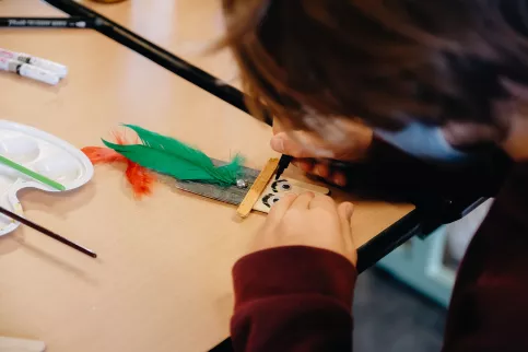 Un élève de maternelle crée un personnage en batonnets de bois pendant un cours d'art plastique.