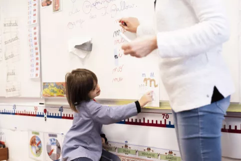 Une élève de maternelle est au tableau pour apprendre l'alphabet.