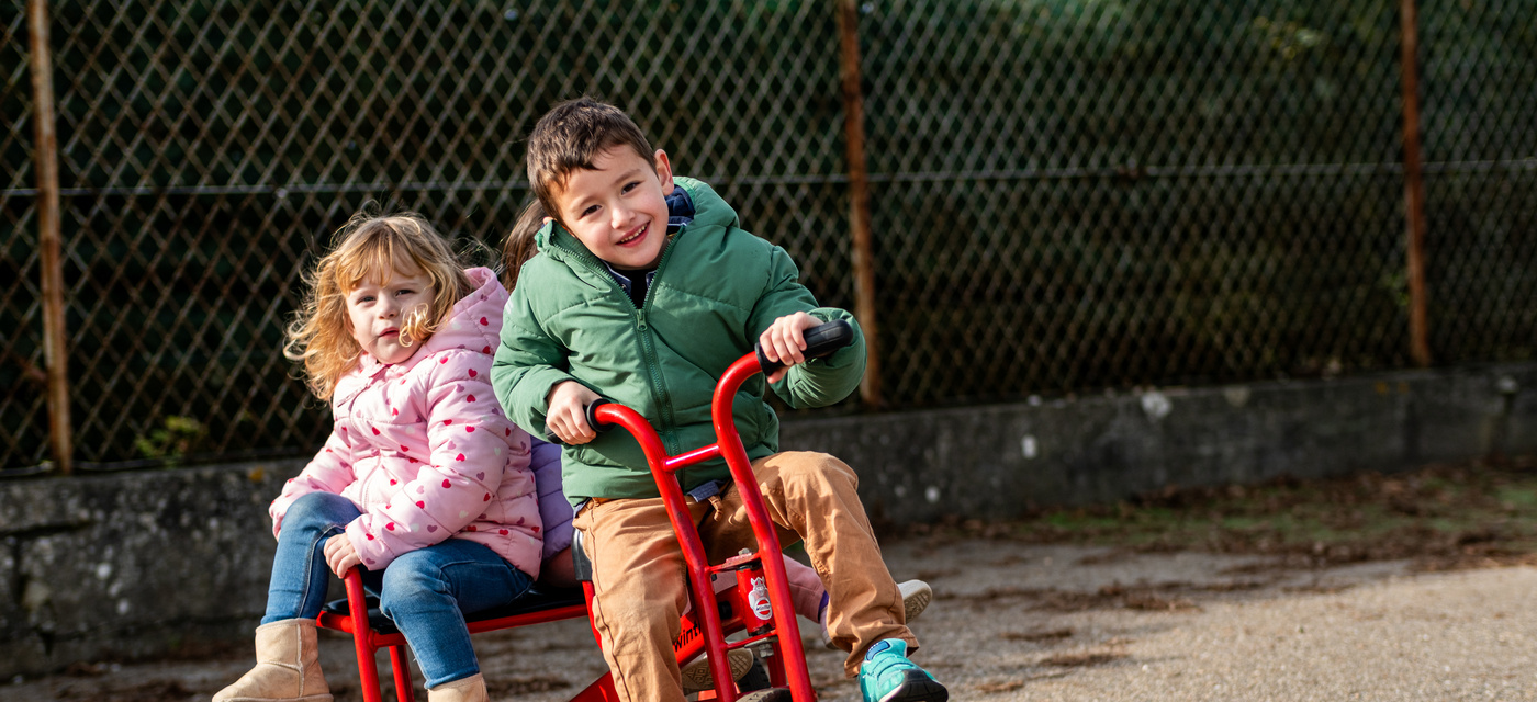 Deux élèves de maternelle jouent sur un vélo dans une cour d'école