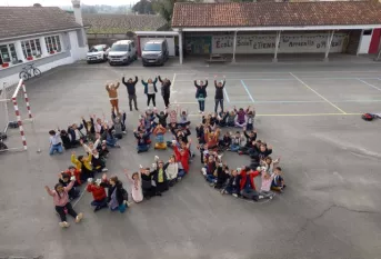 des élèves sont dans une cours d'école. Ils sont assis de façon à former le nombre 156.