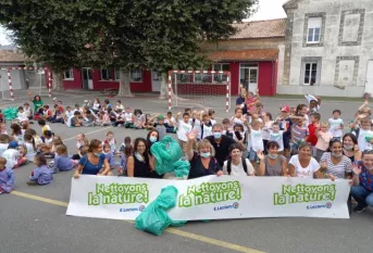 des élèves sont assis dans une cour d'école. Les professeurs sont assis devant avec une banderole "Nettoyons la nature"